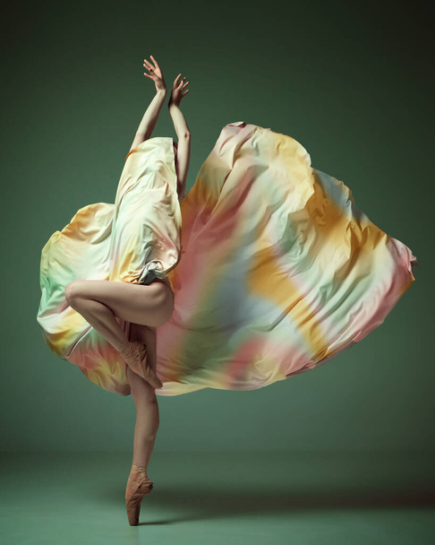 Lábujjhegyen. Egy kecses balerina szivárványruha tánccal, kecses mozdulattal, sötétzöld stúdió háttérrel. A kortárs tánc szépsége. Művészet, mozgás, rugalmasság, inspiráció - Fotó, kép
