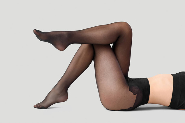 benen van mooie vrouw in zwart panty op lichte achtergrond - Foto, afbeelding
