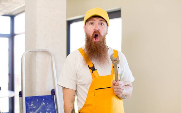 red hair man feeling extremely shocked and surprised repairing home. handyman concept - Foto, immagini