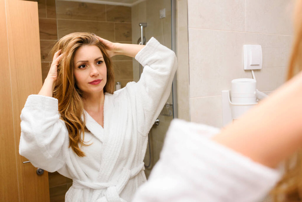 beautiful young woman getting ready, looking at mirror in bathroom - Fotó, kép