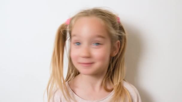 Ein hübsches lachendes, kinderblondes Mädchen von sieben Jahren nickt mit dem Kopf nein. Negativ schüttelt er den Kopf, verwöhnt, lächelt und grimassiert - Filmmaterial, Video