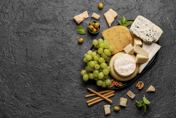 Bandeja con diferentes tipos de sabrosos quesos y uvas sobre fondo oscuro - Foto, Imagen