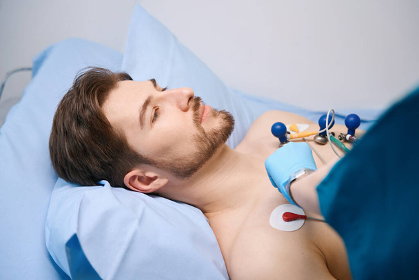 Cardiograph suction cups are attached to patient to take a cardiogram, man lies on hospital bed with a naked torso - Foto, afbeelding