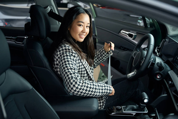 若いアジアの女性が運転席に座ってシートベルトを使って - 写真・画像