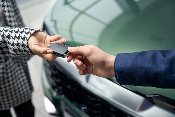 Nainen ottaa auton avaimet mieheltä työpuvussa, ihmiset seisovat kiiltävän uuden auton edessä. - Valokuva, kuva