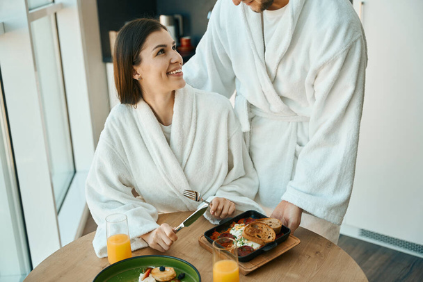 Caring young husband treats his sweet wife to breakfast in a cozy atmosphere, the guys in comfortable bathrobes - Fotoğraf, Görsel