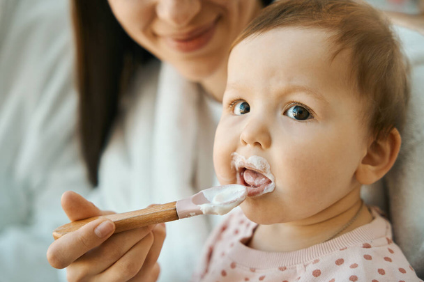 Smiling woman feeding a small child with a small spoon, the baby has chubby cheeks - Foto, imagen