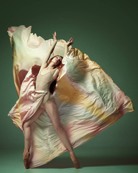 Jedna půvabná baletka v duhových šatech tančící půvabným pohybem na tmavozeleném pozadí studia. Krása současného tance. Umění, pohyb, flexibilita, inspirace, koncepce elegance - Fotografie, Obrázek