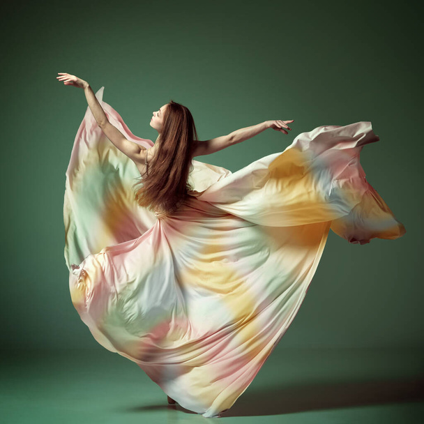 Ballet moderne avec robe en soie. Une belle ballerine, jeune fille dansant gracieusement avec du tissu sur fond de studio vert foncé. Concept de beauté ballet classique art, esthétique - Photo, image