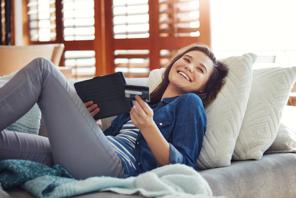 Oh comme j'adore le jour de paie. une jeune femme séduisante utilisant sa tablette pour magasiner en ligne tout en se relaxant sur le canapé à la maison - Photo, image