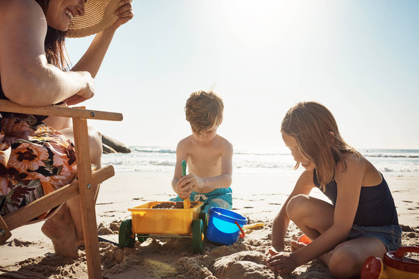 La plage, aire de jeux d'été. un adorable petit garçon et fille jouant avec des jouets de plage dans le sable tandis que leur mère regarde - Photo, image