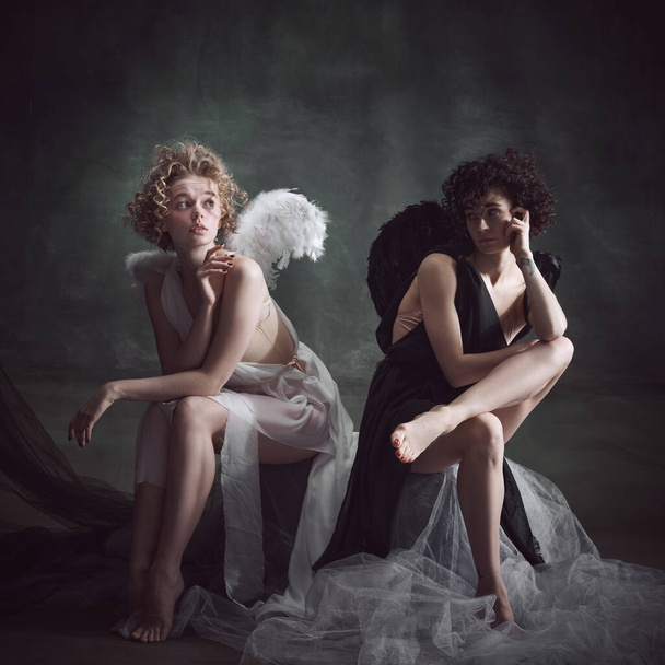 Portrait of two women, queens, angel and demon against dark, green, vintage background. Balance of human being. Concept of history, remake, good and bad, creative photography, fashion - Fotografie, Obrázek