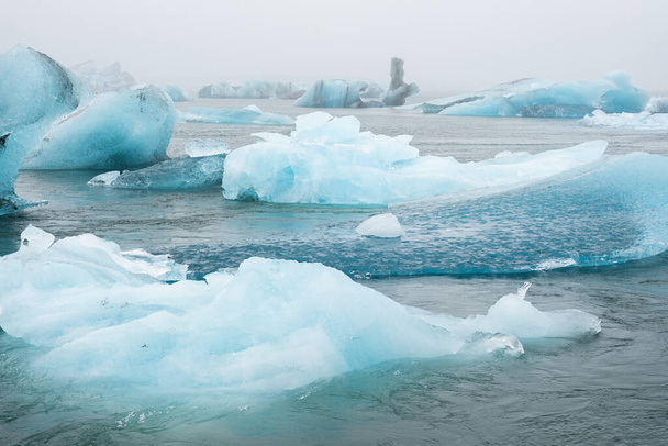 Błękitne góry lodowe w oceanie. Lodowiec dryfuje przy spokojnej wodzie. Czyste kawałki lodu z topniejącego lodowca. Lodowaty Zimowy Krajobraz. Pogoda w Islandia.. Wysokiej jakości zdjęcie - Zdjęcie, obraz