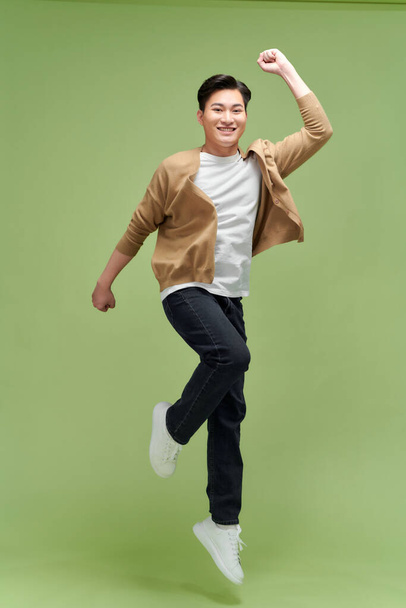 Счастливый взволнованный молодой азиат прыгает изолированный на зеленом фоне студии - Фото, изображение