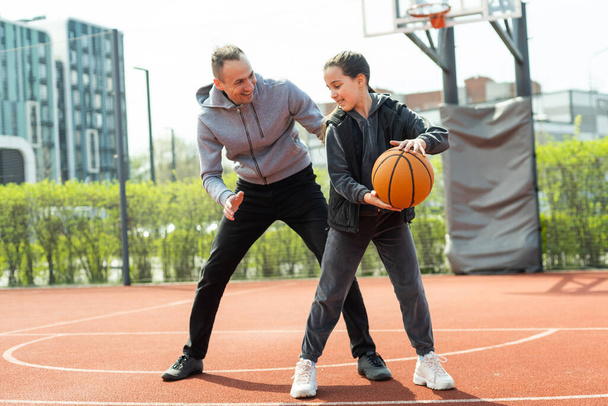 Happy father and teen daughter outside at basketball court - Фото, изображение