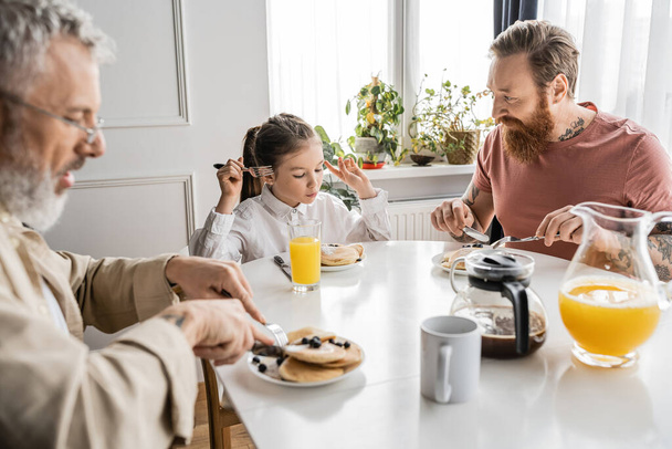 preteen girl having breakfast with gay parents at home in morning  - Photo, Image