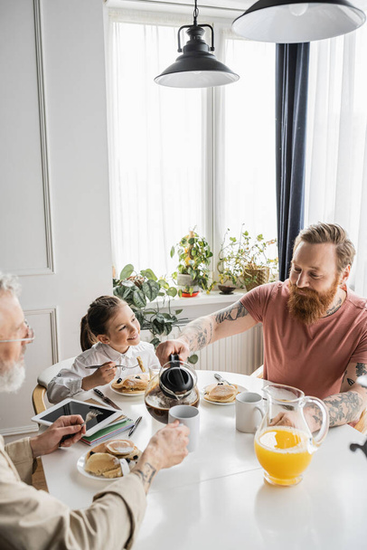 Gay man pouring coffee near partner and daughter during breakfast at home  - Valokuva, kuva