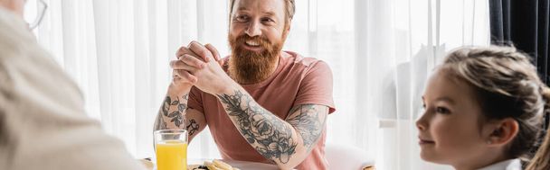 Cheerful gay man sitting near breakfast and parents at home, banner  - Фото, изображение