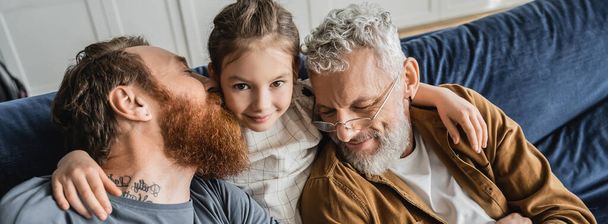 High angle view of carefree girl hugging same sex parents on couch at home, banner  - Photo, Image