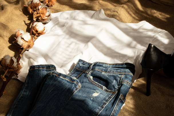 T-shirt branca e jeans mentira em uma serapilheira marrom e um ramo de algodão e sapatos, roupas de moda e sapatos para mulheres - Foto, Imagem