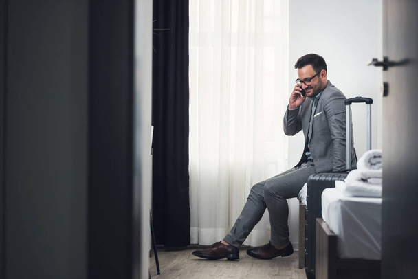 Επιχειρηματίας που χρησιμοποιεί smartphone στο δωμάτιο του ξενοδοχείου. Ταξιδεύοντας για εργασία. - Φωτογραφία, εικόνα