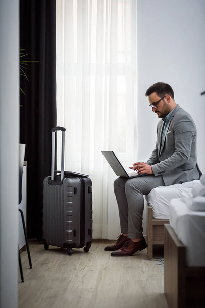 Empresario usando computadora portátil, trabajando en su habitación de hotel. Viajar por trabajo. - Foto, Imagen
