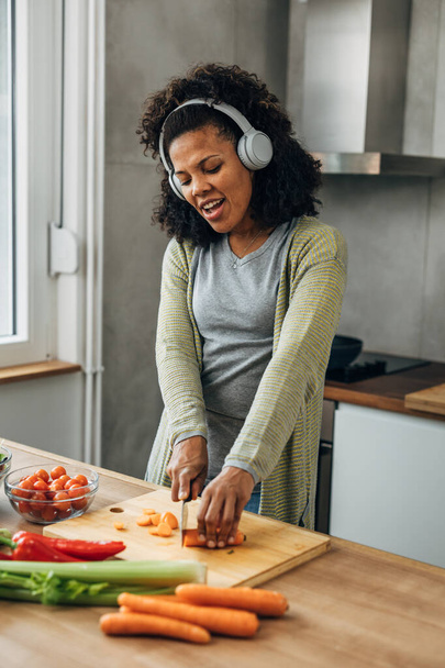 A cheerful Multiracial woman is singing while cooking at home. - Foto, afbeelding
