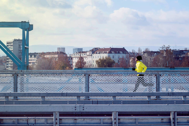 Attractive fit man running fast along big modern bridge. Exercising, Jogging, Sport, Winter. Male athlete running. - Valokuva, kuva
