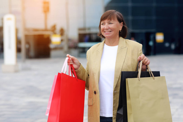 Seasonal Sales. Happy adult woman with shopping bags. Middle ages female after shopping on shopping mall background. Purchases, discounts, sale concept. Online shopping concept, Black friday. mockup. - Foto, afbeelding