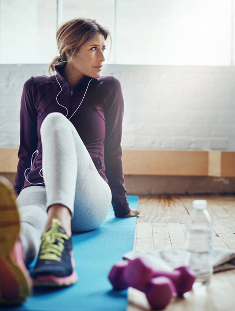Checking off her fitness goals one by one. an attractive young woman listening to music while working out at home - Photo, image