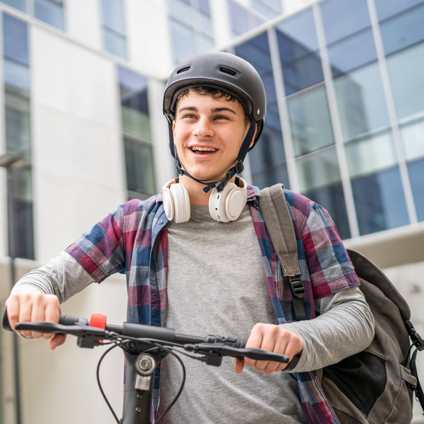 Un giovane uomo caucasico maschio adolescente generazione Z con scossa elettrica spingere scooter presso l'edificio moderno in città eco modo di trasporto concetto copia spazio - Foto, immagini