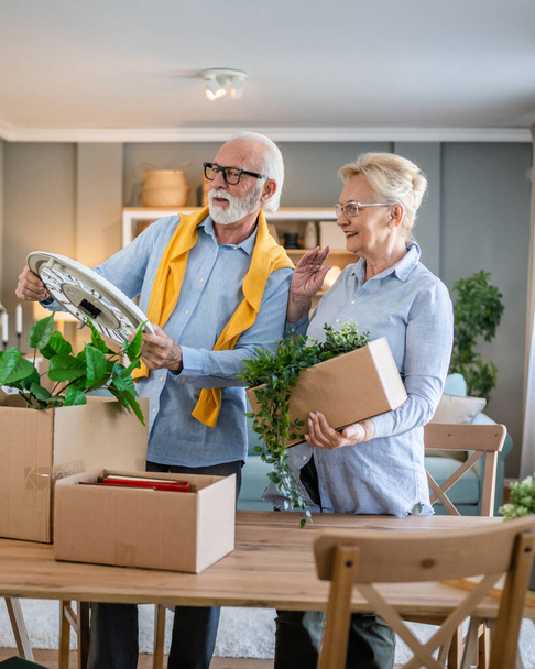family senior couple man woman husband and wife pensioner grandfather grandmother moving in new apartment taking their stuff belongings and plants in or out of boxes packing or unpacking real people - Fotografie, Obrázek