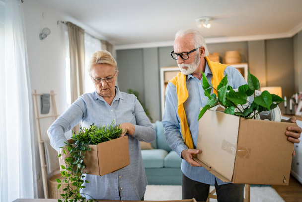 family senior couple man woman husband and wife pensioner grandfather grandmother moving in new apartment taking their stuff belongings and plants in or out of boxes packing or unpacking real people - Photo, Image