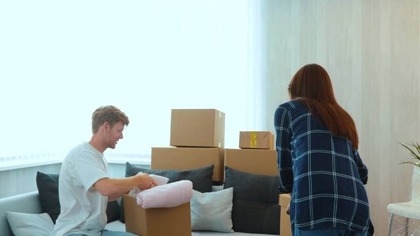 Caucasian joyful couple man and woman just moved in a new apartment unpacking their stuff and clothes. Cardboard boxes in room. Excited homeowners. Moving day. Happy wife and husband in own house - 写真・画像