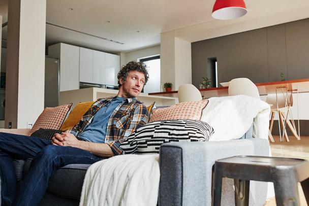 Contemplando qué hacer el resto del día. un hombre maduro guapo relajándose en el sofá en casa - Foto, Imagen