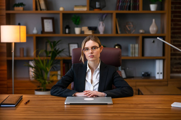 Masada dizüstü bilgisayarla oturan beyaz gömlekli ofis müdürü kadın. Ofisteki kameraya bakan gülümseyen ofis çalışanı. İş kavramı - Fotoğraf, Görsel