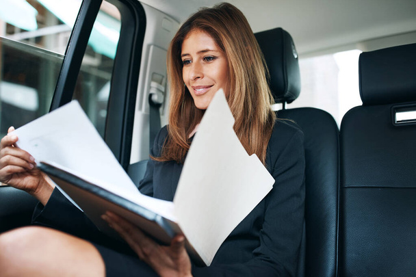 9. Eine reife Geschäftsfrau, die auf dem Rücksitz eines Autos Papierkram erledigen muss - Foto, Bild