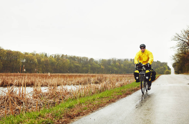 He wont let the weather win. Full length shot of a male cyclist enjoying a bike ride on a wet winters morning - Photo, Image