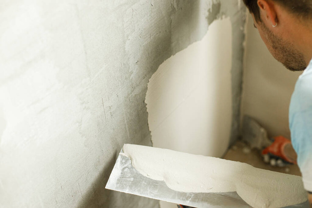 Tamirci duvarları alçıtaşı alçı ve malayla kaplıyor. Ev ve ev yenileme konsepti. İşçi ellerini spatula ve sıva ile kapatın. - Fotoğraf, Görsel