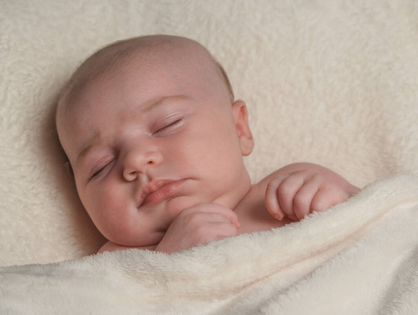 Portrait of newborn baby girl sleeping on her back, covered with a cream blanket. - Photo, Image