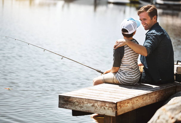 Te enseñaré todos los trucos de pesca, hijo mío. Vista trasera de un padre y su pequeño hijo pescando juntos - Foto, Imagen