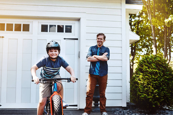 Μπαμπάδες περήφανοι για τις ικανότητες που δίδαξε στο γιο του. Ένα νεαρό αγόρι να κάνει ποδήλατο με τον πατέρα του στο βάθος. - Φωτογραφία, εικόνα