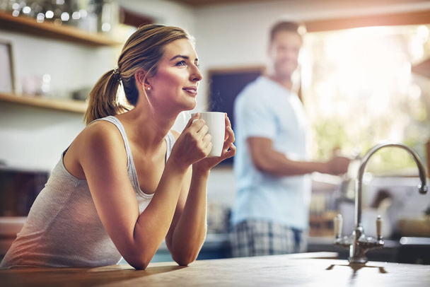 Koffie helpt me mijn dag te plannen. een jonge vrouw het hebben van haar ochtend koffie met haar vriendje staan in de achtergrond - Foto, afbeelding