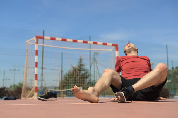 Un homme de 40 ans s'allonge sur le terrain de football avec une jambe blessée, une articulation enflée, levant les yeux et criant concept de risque. Espace de copie. Un arrière-plan flou. Photo de haute qualité - Photo, image