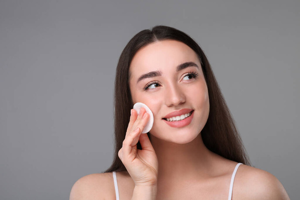 Beautiful woman removing makeup with cotton pad on gray background - Foto, Imagem