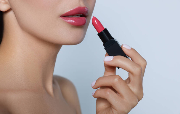 Young woman with beautiful makeup holding glossy lipstick on light gray background, closeup - Φωτογραφία, εικόνα