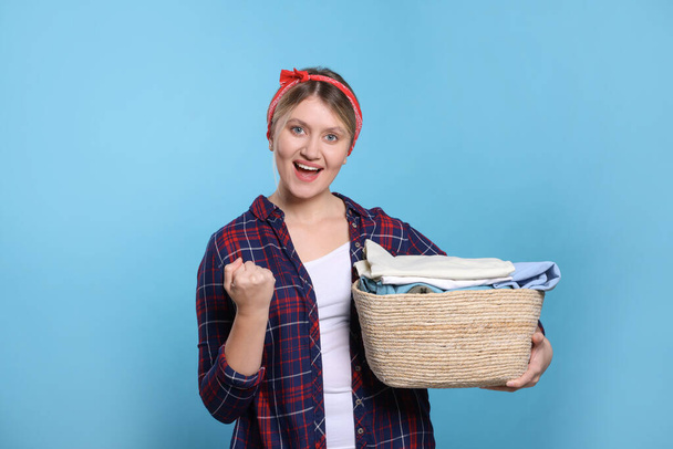 Emotional woman with basket full of laundry on light blue background - Photo, Image
