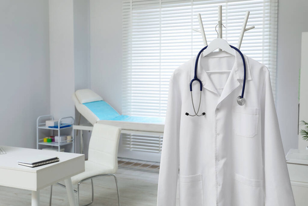 White doctor's gown and stethoscope hanging on rack in clinic. Space for text - Fotografie, Obrázek
