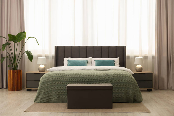 Comfortable bed, bedside tables and ottoman in bedroom - Foto, afbeelding
