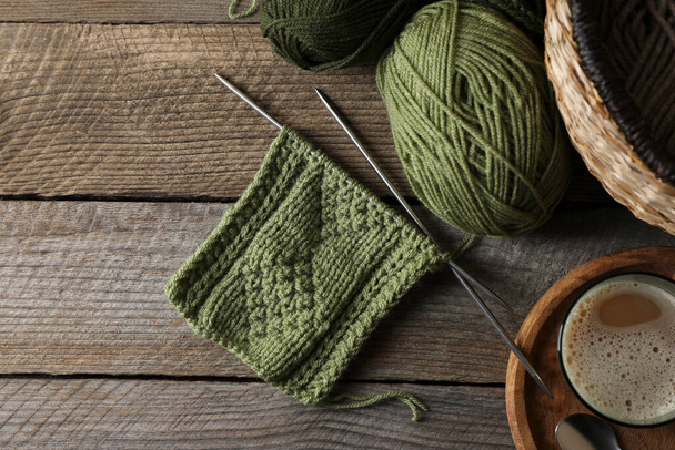 Soft green woolen yarn, knitting, needles and glass of drink on wooden table, flat lay. Space for text - Фото, изображение